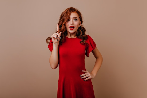 Mujer alegre y bien vestida con cabello pelirrojo que expresa emociones sinceras. Chica de buen humor en vestido blanco posando.