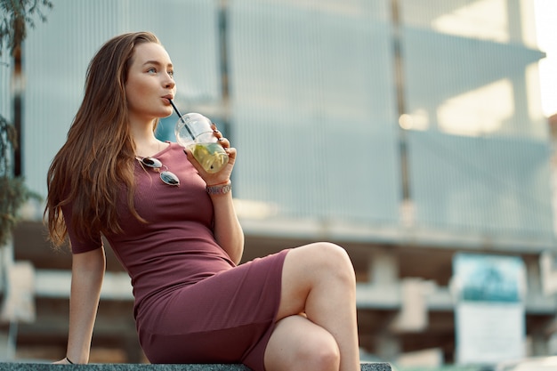 Mujer alegre en la calle bebiendo mañana refrescante bebida