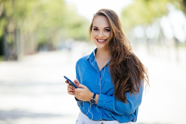 Mujer alegre en la calle usa su teléfono inteligente. Joven empresaria con teléfono en la calle.