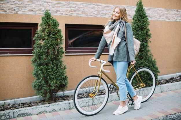 Mujer alegre caminando con bicicleta cerca del edificio