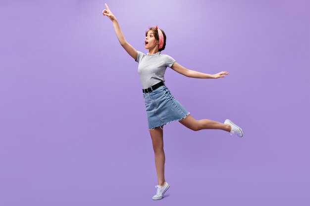Mujer alegre en camiseta gris y falda posando.n fondo aislado. Encantadora chica encantadora en traje de moda de verano saltando.
