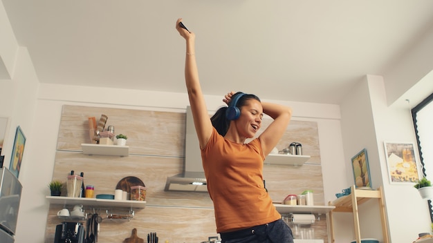 Mujer alegre cantando en la cocina por la mañana. Ama de casa enérgica, positiva, alegre, divertida y linda bailando sola en la casa. Entretenimiento y ocio solo en casa.