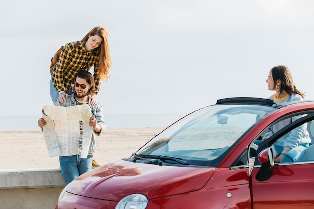Foto gratuita mujer alegre cerca del hombre que mira el mapa y la señora que se inclina hacia fuera del coche