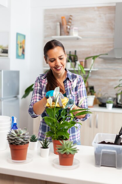 Mujer alegre cuidando de las flores en casa en una acogedora cocina. Usando tierra fertil con pala en maceta, maceta de cerámica blanca y plantas preparadas para replantar para la decoración de la casa cuidándolas