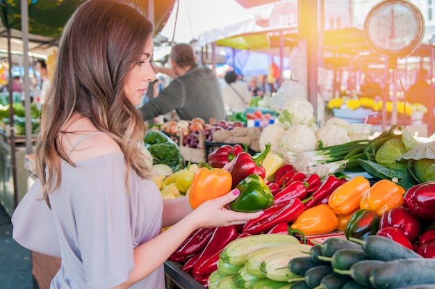 Mujer alegre elegir el pimentón verde y rojo en el supermercado. Compras. Mujer que elige la fruta de la comida bio pimienta paprica en el mercado verde