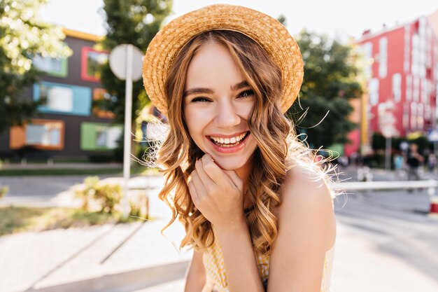 Mujer alegre emocionada jugando durante el fin de semana de verano. Encantadora modelo femenina rizada en traje de moda disfrutando de la sesión de fotos.