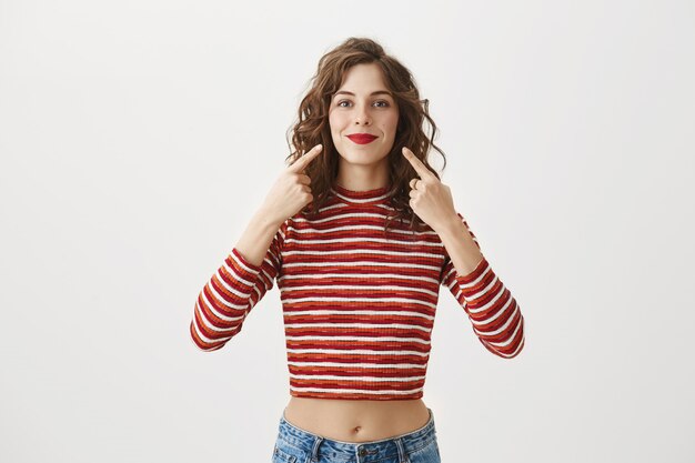 Mujer alegre feliz apuntando a su sonrisa o lápiz labial rojo