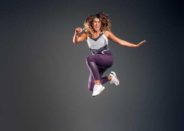 Foto gratuita una mujer alegre y feliz muestra su actuación en el estudio fotográfico sobre el fondo gris.