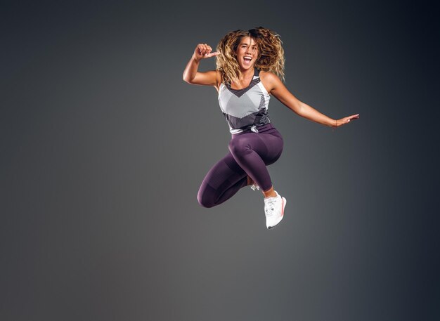 Una mujer alegre y feliz muestra su actuación en el estudio fotográfico sobre el fondo gris.