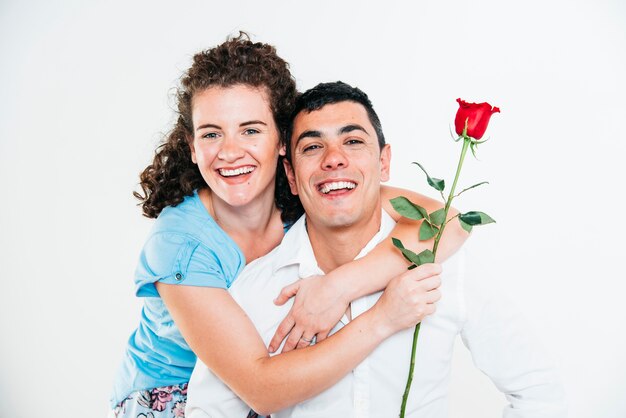 Mujer alegre con flor abrazando a hombre sonriente