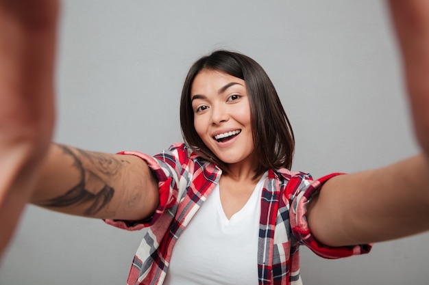 Mujer alegre hacer selfie sobre pared gris.