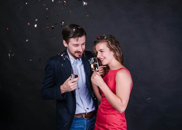 Mujer alegre joven cerca de hombre con vasos de bebida entre tirar confeti