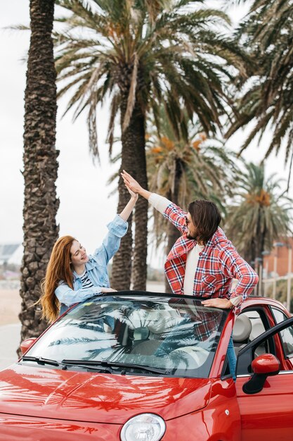 Mujer alegre joven y hombre dando alta cinco de coche