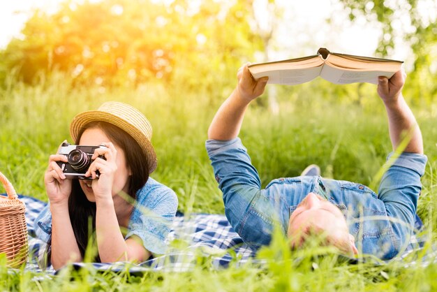 Mujer alegre joven que toma el libro de lectura de la foto y del hombre en hierba