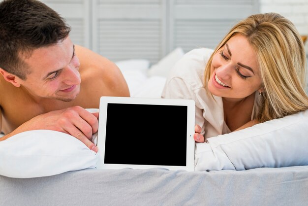 Mujer alegre y joven sonriente con marco de fotos en la cama