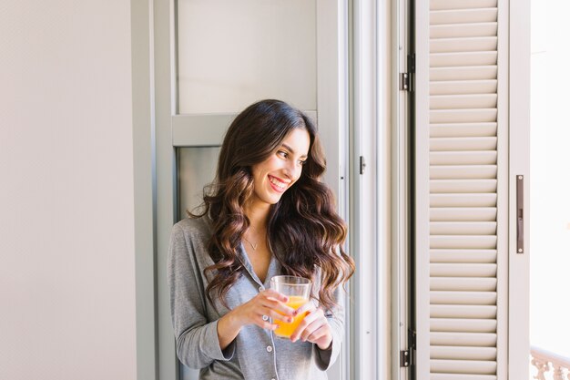 Mujer alegre con jugo junto a la ventana