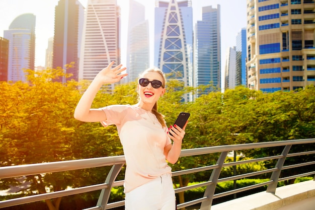 La mujer alegre con los labios rojos levanta su mano para arriba mientras que ella se coloca en puente antes de rascacielos