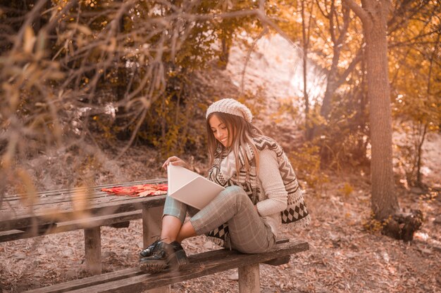 Mujer alegre leyendo cerca de la mesa en el bosque de otoño