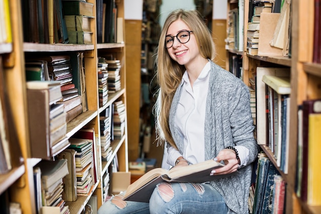 Mujer alegre con libro en biblioteca