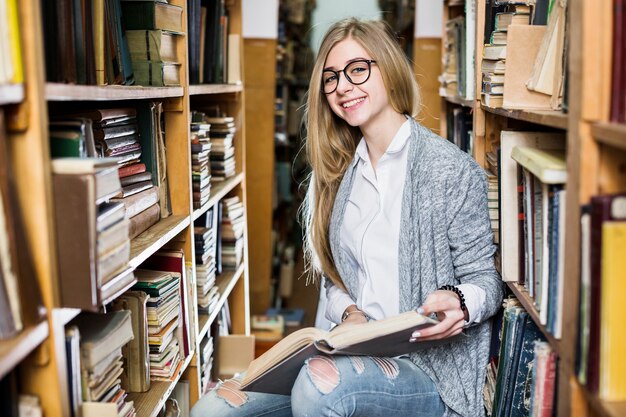 Mujer alegre con libro en biblioteca