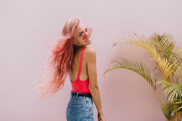 Foto gratuita mujer alegre en pantalones cortos de mezclilla posando junto a la palmera.