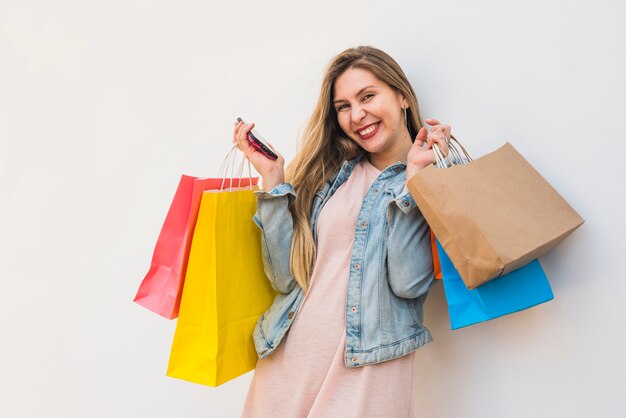 Mujer alegre de pie con teléfono inteligente y bolsas de compras