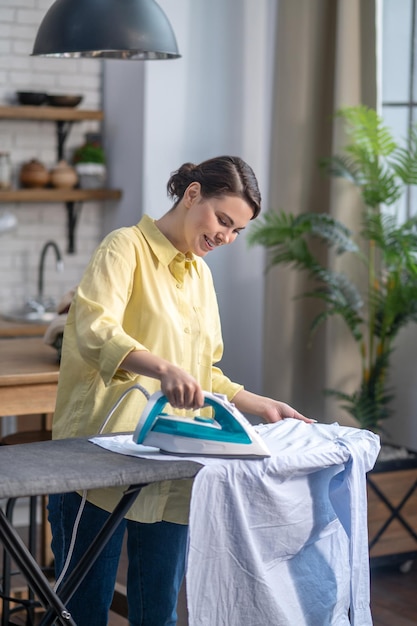 Mujer alegre planchando ropa arrugada en la tabla de planchar