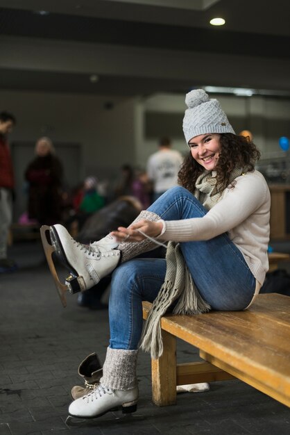 Mujer alegre que ata patines de hielo