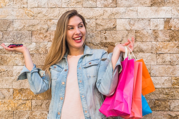 Mujer alegre que se coloca con los bolsos de compras brillantes