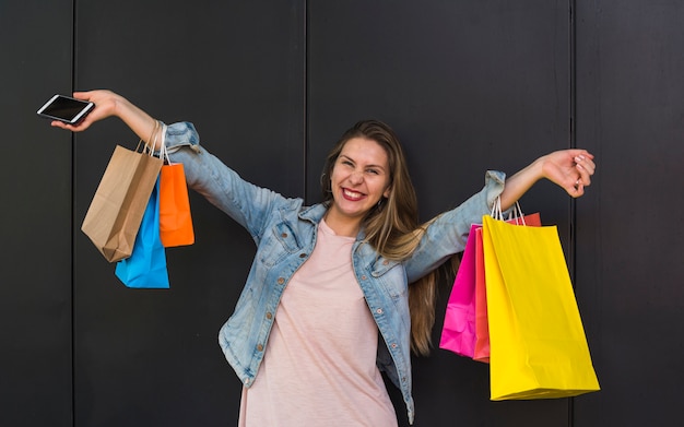 Mujer alegre que se coloca con los bolsos de compras coloridos