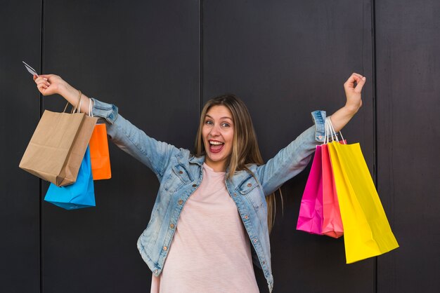 Mujer alegre que se coloca con los bolsos de compras coloridos