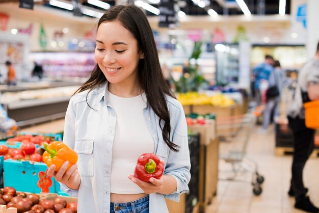 Mujer alegre que elige el paprika en tienda de comestibles