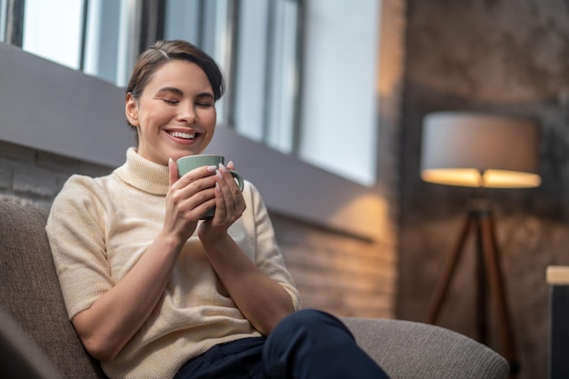 Foto gratuita mujer alegre que inhala el aroma de la bebida en sus manos