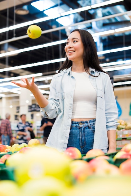 Mujer alegre que lanza para arriba la manzana en tienda de comestibles