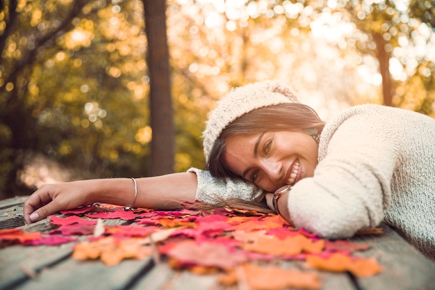 Foto gratuita mujer alegre que miente en la tabla con las hojas de otoño