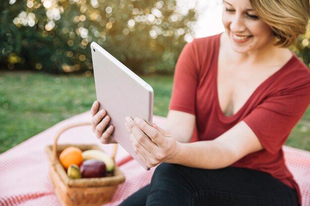 Mujer alegre que mira la tableta en comida campestre