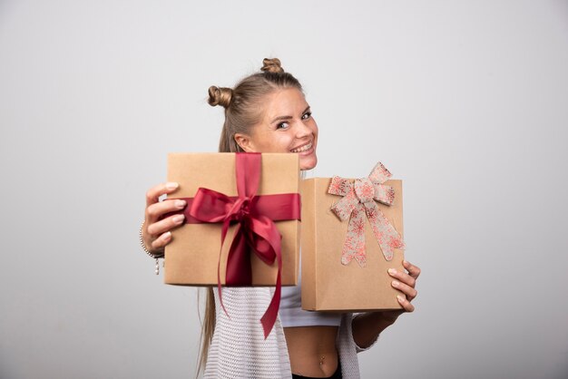 Mujer alegre que muestra cajas de regalo sobre fondo gris.