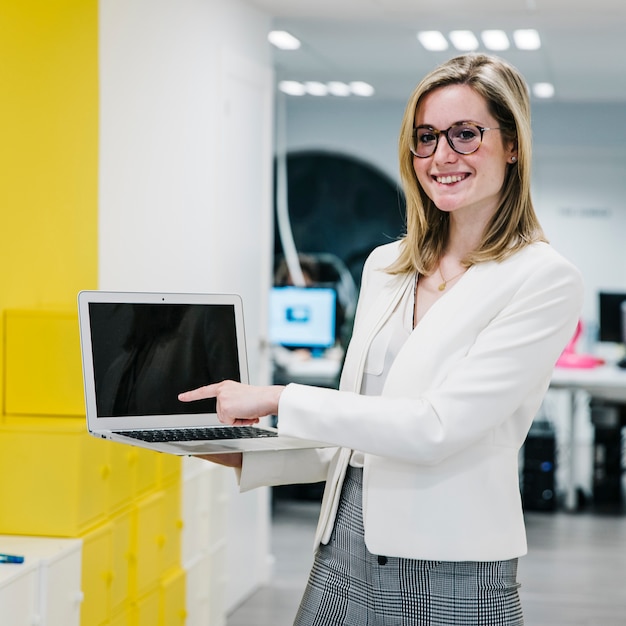 Foto gratuita mujer alegre que señala en la exhibición de la computadora portátil