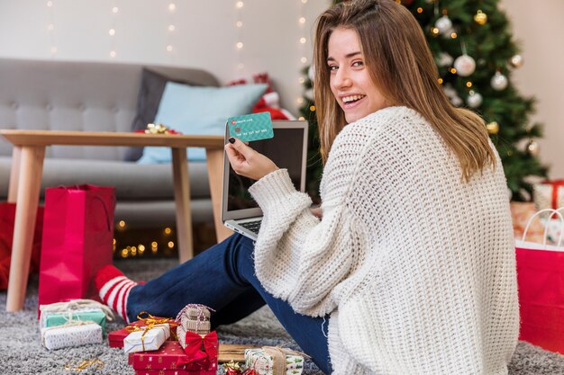 Mujer alegre que sostiene la tarjeta en los regalos de la Navidad