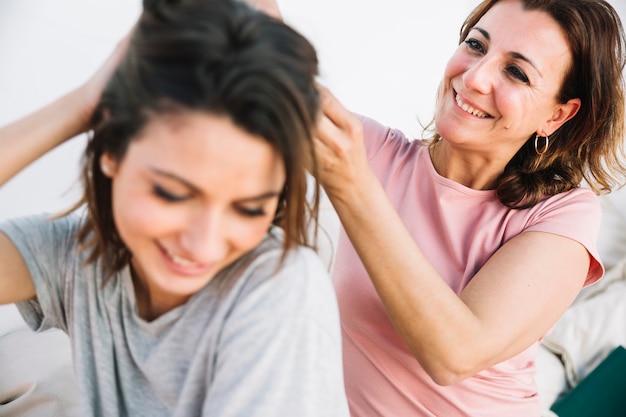 Mujer alegre que trenza el pelo de la mujer