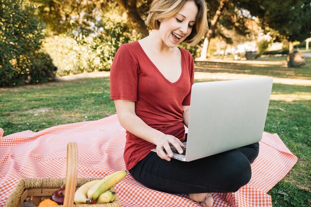 Mujer alegre que usa la computadora portátil en comida campestre