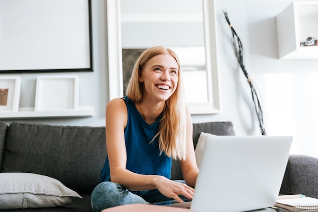 Mujer alegre que usa la computadora portátil y riéndose en casa