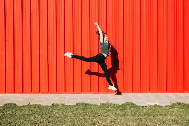 Mujer alegre saltando cerca de la pared roja