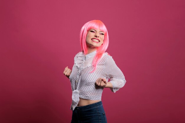 Mujer alegre y segura de sí misma celebrando una gran victoria y éxito, posando frente a la cámara sobre un fondo rosa. Sentirse feliz y emocionado por el logro y el maravilloso triunfo, estilo ganador.