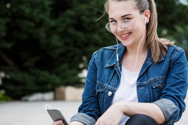 Foto gratuita mujer alegre con smartphone sentado en la acera