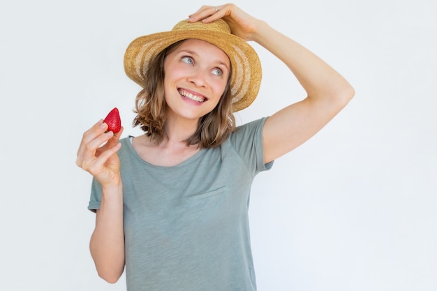 Mujer alegre en sombrero con fresa madura y sonriente