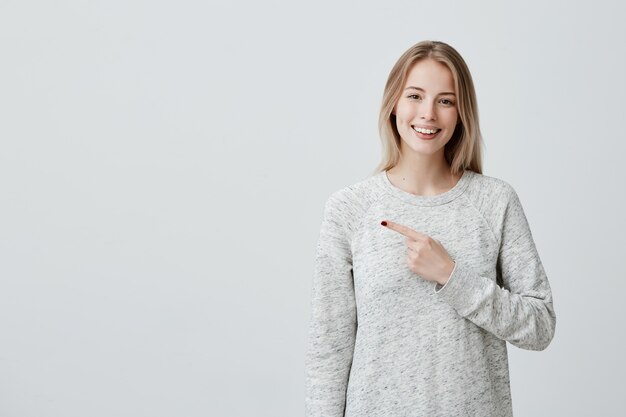 Mujer alegre sonriente que señala con el dedo en copyspace