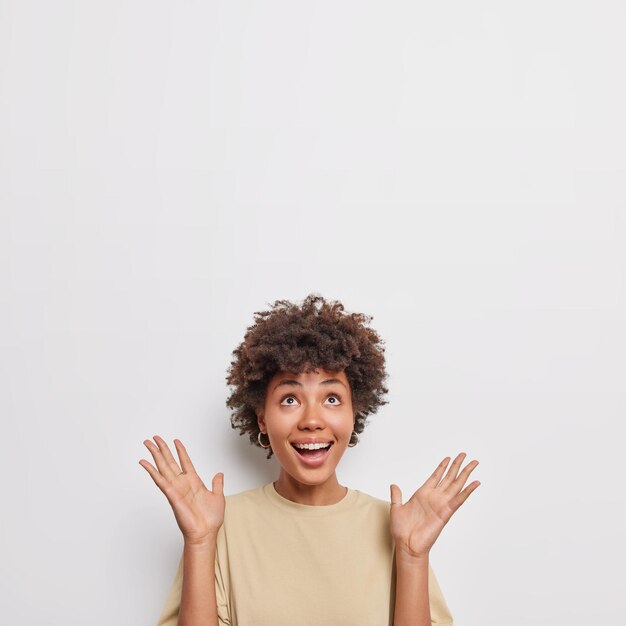 Mujer alegre sorprendida mantiene la palma levantada enfocada por encima de las risas felizmente vestida con una camiseta marrón casual feliz de notar que el producto impresionante reacciona a la sugerencia de una buena venta. Copie el espacio contra la pared blanca