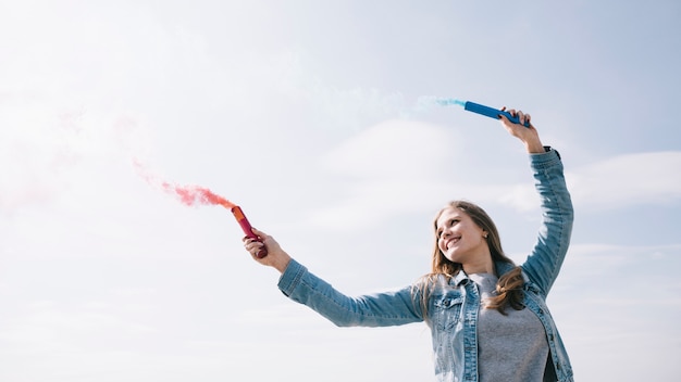 Mujer alegre sosteniendo humo destellos en manos extendidas