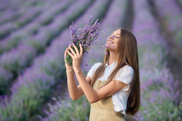 Mujer alegre sosteniendo ramo en campo de lavanda